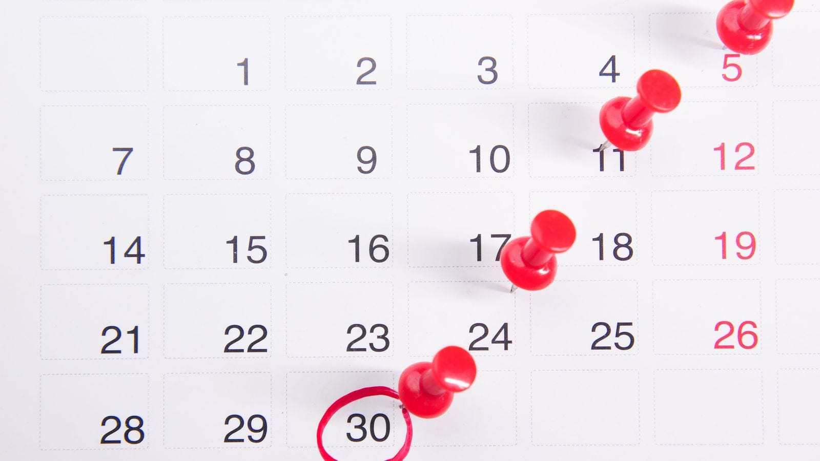 A calendar page marked with four red push pins and one date circled in red pen